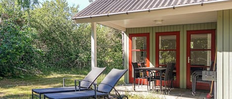 Une petite maison avec une véranda, deux fauteuils, une table et des chaises.
