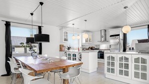 A modern kitchen with white cabinetry, a wooden dining table, and pendant lights.