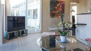 A modern living room with a large TV, a glass coffee table, and a potted orchid. - 3 bedroom amazing home in Nexø (Nexø)