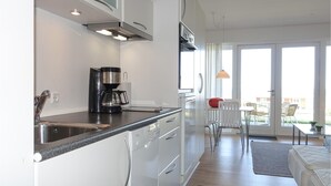 Una cucina moderna con una macchina da caffè, elettrodomestici in acciaio inossidabile e una porta scorrevole in vetro che dà su un balcone con posti a sedere esterni.
