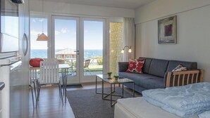 Una stanza moderna con divano, letto, tavolino in vetro e vista mare tramite ampie finestre.