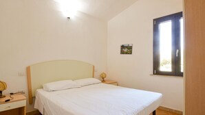 A bedroom with a bed, a nightstand, a lamp, a small table, and a window. - Nice home in Costa Rei with WiFi (Costa Rei)