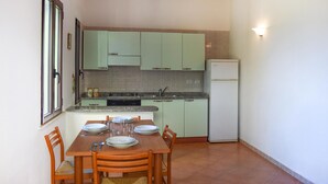 A compact kitchen with green cabinets, a white refrigerator, and a dining table set for four. - Nice home in Costa Rei with WiFi (Costa Rei)