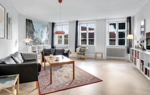 Relax in a spacious living area with a leather sofa, armchair, and wooden coffee table, surrounded by books and natural light.