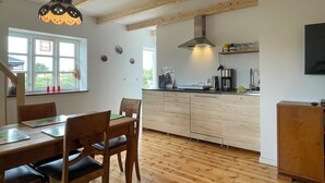 A modern kitchen with wooden cabinets, a dining area with a table and chairs, and a large window with curtains. - Nice apartment in østermarie with WiFi (Østermarie)