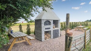A stone-built outdoor kitchen with a chimney, a wooden table, and a rustic fence. - Nice apartment in østermarie with WiFi (Østermarie)