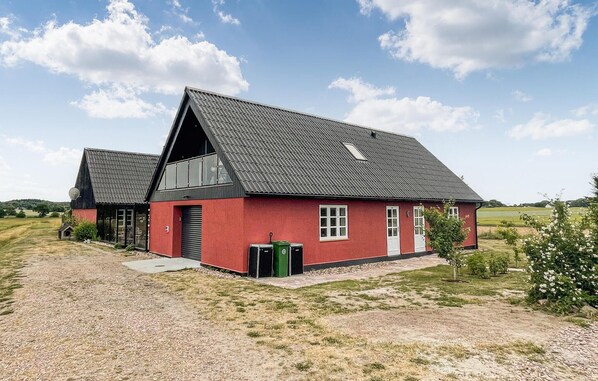 Ein rotes Haus mit geneigtem Dach, einer Satellitenschüssel und einer grünen Mülltonne davor.