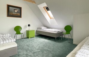 Ein kleines, modernes Schlafzimmer mit schrägen Wänden, einem Einzelbett, zwei grünen Stühlen, einem kleinen grünen Tisch mit einer Lampe und einem gerahmten Bild an der Wand.