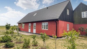 A red house with a dark roof and white windows, surrounded by a grassy area with young trees. - Nice apartment in østermarie with WiFi (Østermarie)