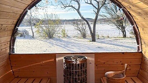A wooden cabin with a large window, a fireplace, and a wooden bench. - Nice apartment in østermarie with WiFi (Østermarie)
