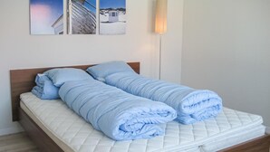 Ein ordentlich bezogenes Bett mit einer gesteppten Matratze und blauer Bettwäsche, einem Holz-Kopfteil und einer Wandlampe.