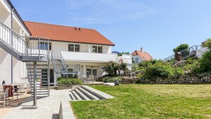 Ein zweigeschossiges Gebäude mit rotem Ziegeldach, einer Treppe, die zu einem Balkon führt, und einem grünen Rasen.