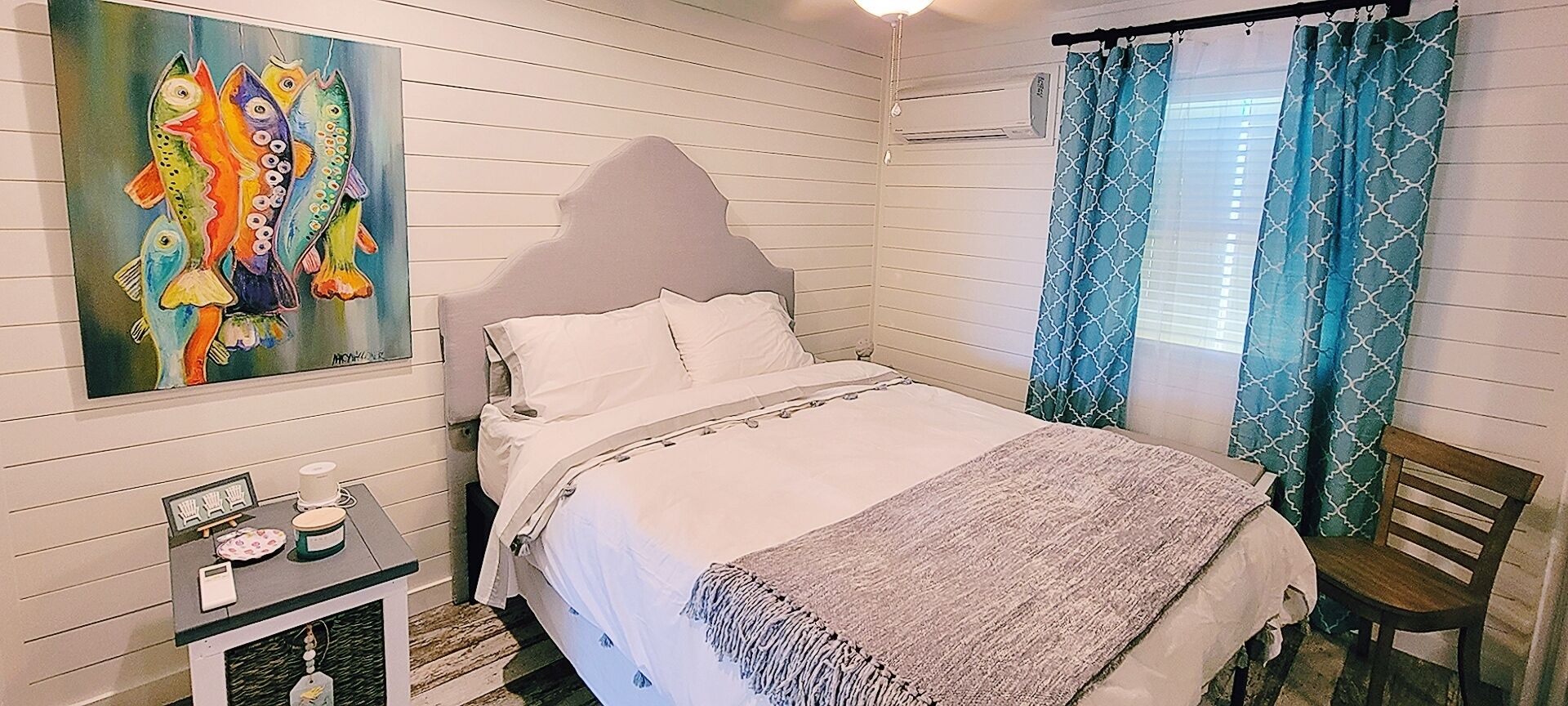 A bedroom with a bed, a nightstand, a chair, a painting, and curtains.