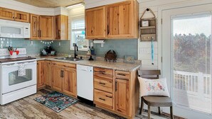 A kitchen with wooden cabinets, a white stove, a dishwasher, and a window with blinds. - BAY-CAY Getaway, Beaching, Casinos, Swim, Grill, Chill, Memories! (Bay St. Louis)