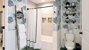 A bathroom with a bathtub, toilet, and shower curtain. There are towels hanging on a rack and a sign with a monogram on the wall. - BAY-CAY Getaway, Beaching, Casinos, Swim, Grill, Chill, Memories! (Bay St. Louis)