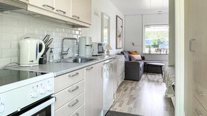A compact kitchen with a stove, sink, and modern appliances. A small dining area with a table and chairs is visible in the background. - Amazing apartment in Nexø with sauna (Nexø)
