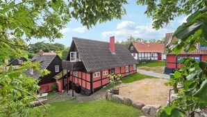 Une maison traditionnelle à colombages, dotée d’un toit en pente et d’une cheminée bien visible, entourée d’une pelouse bien entretenue et d’un chemin en pierre.