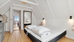 Une chambre avec un plafond en pente, un lit avec une literie blanche, une commode en bois et un miroir.