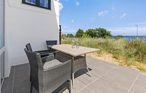 A patio with wicker furniture and a table, overlooking a grassy area and the sea.