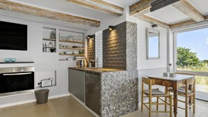 Eine moderne Küche mit Steinrückwand, Holzbalken und Blick ins Freie.