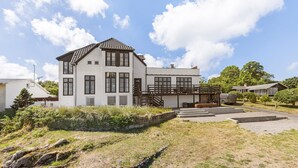 Ein zweistöckiges Haus mit Balkon, einer Steinsichtmauer und einem gepflasterten Auffahrt.