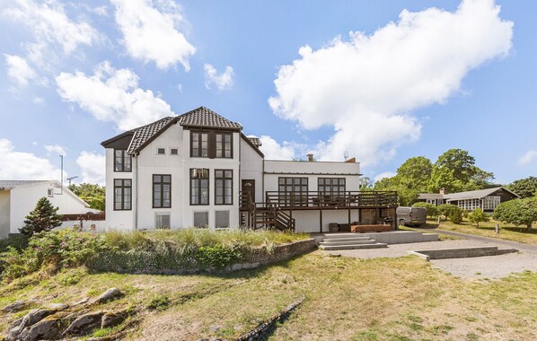 A two-story house with a balcony, a stone retaining wall, and a paved driveway.