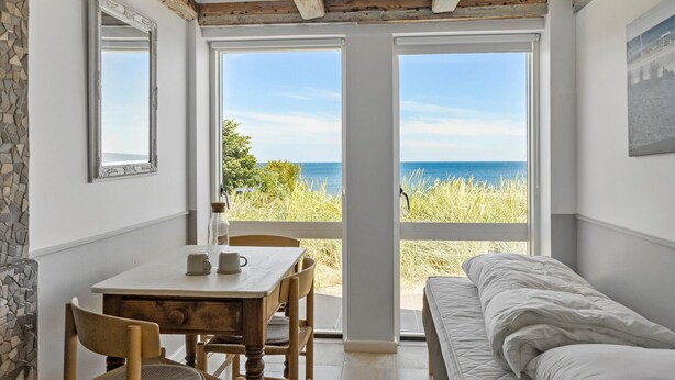 Ein Zimmer mit Tisch und Stühlen, einem Bett und großen Fenstern mit Meerblick.
