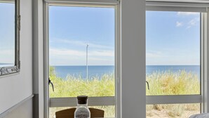 Ein Zimmer mit Blick auf das Meer und Wiesen. Auf dem Tisch steht eine Flasche.