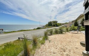 A coastal road with a beach on one side, a bus stop, and a building with a balcony overlooking the road.