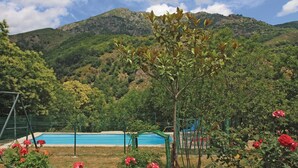 A pool area with a mountain backdrop, surrounded by lush greenery and flowering plants.