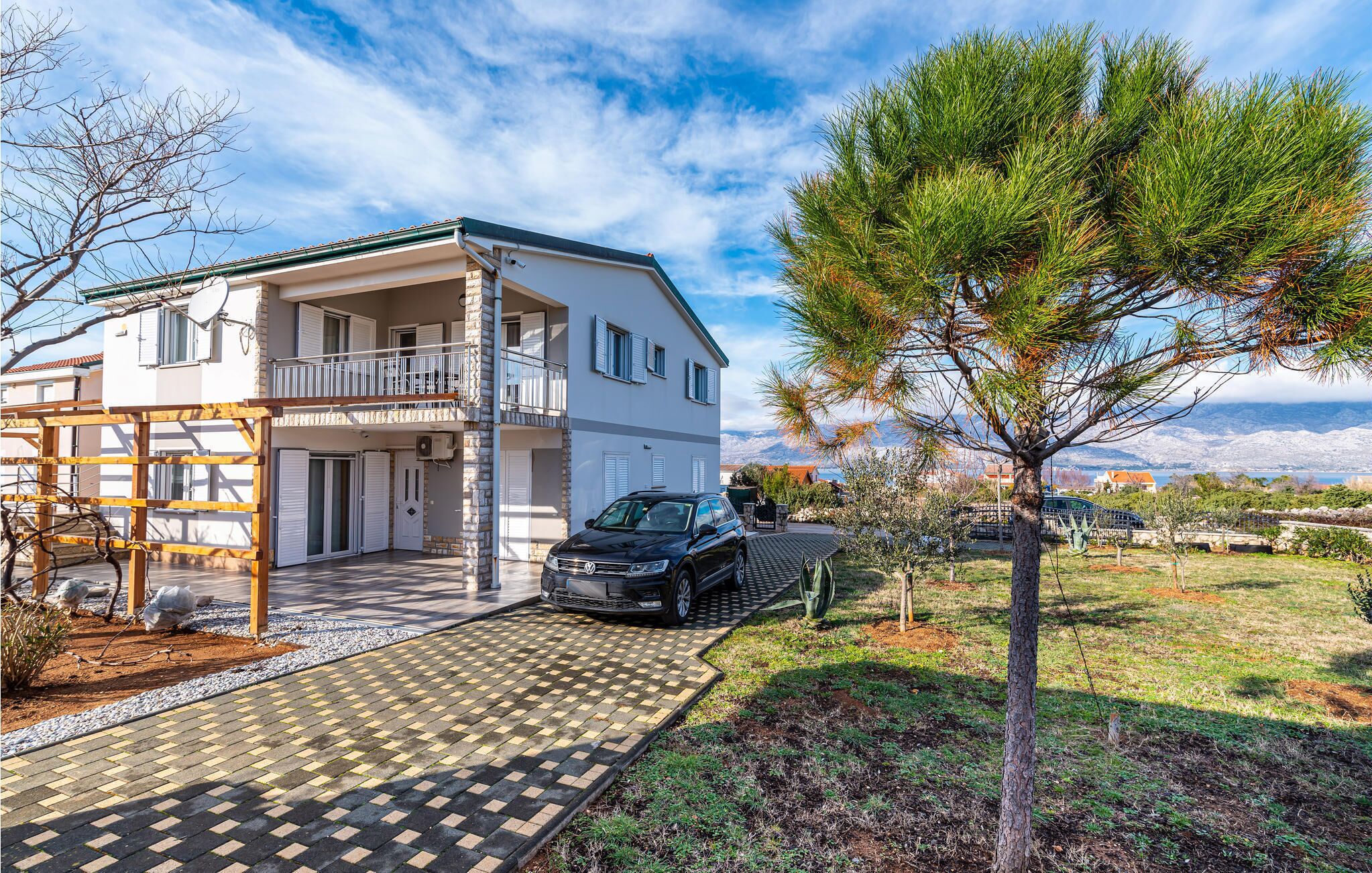 Ein zweistöckiges Haus mit Balkon, einem Auto auf der Auffahrt und einem Baum im Vorgarten.