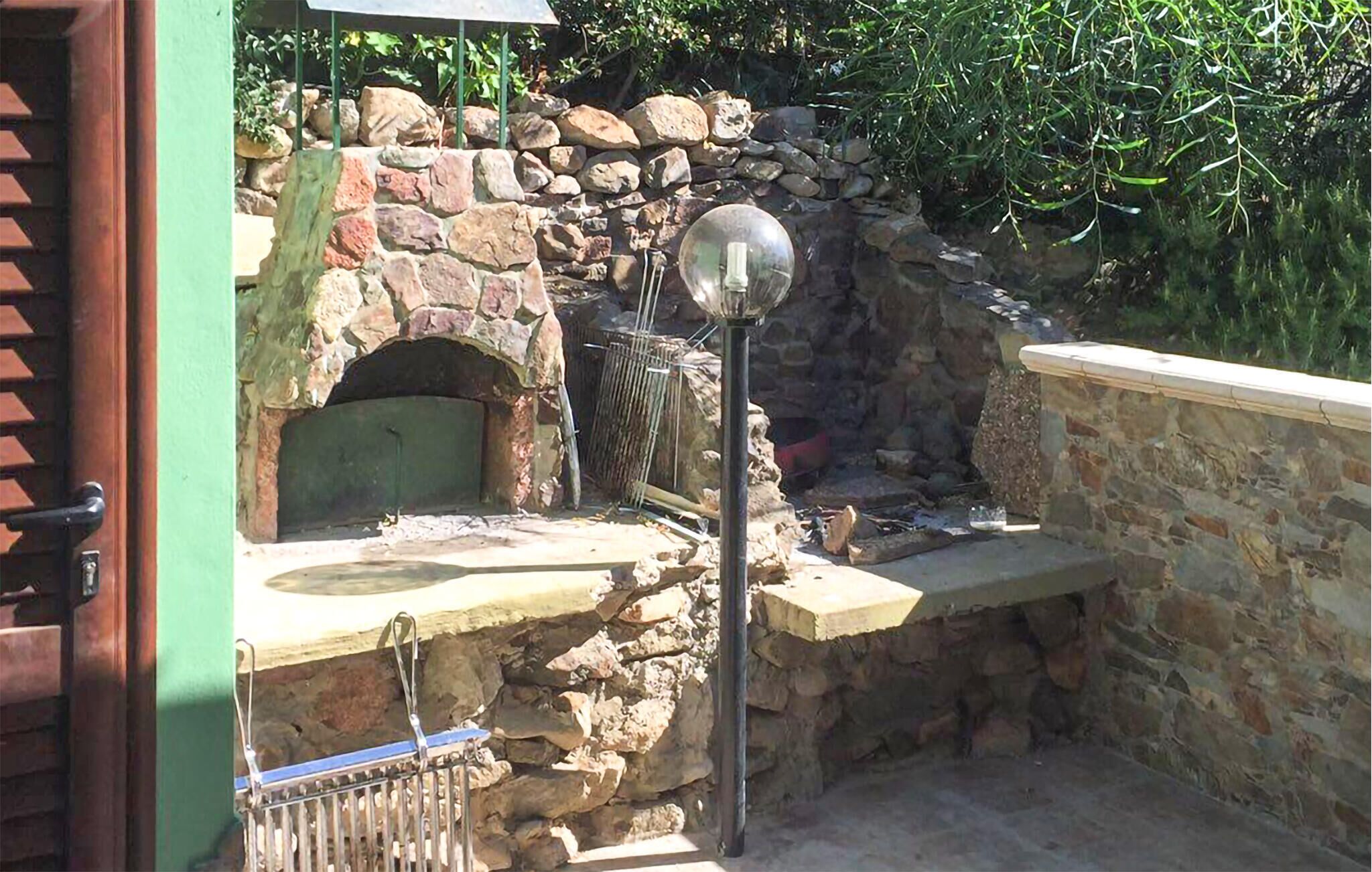 A stone-built outdoor kitchen with a pizza oven, a sink, and a metal rack.