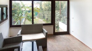 A balcony with wicker furniture, a glass door leading outside, and a view of greenery and buildings. - 2 bedroom gorgeous home in Costa Rei (Costa Rei)