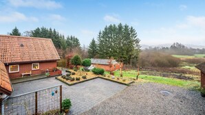 Ein Wohnhaus mit befestigter Auffahrt, einem eingezäunten Garten und Blick auf eine bewaldete Landschaft.