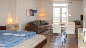 Hotelkamer met een bed, een bank, een eettafel met stoelen, een televisie en een raam met jaloezieën.