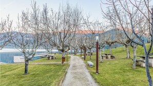 A pathway lined with trees and benches, leading towards a body of water with a bridge in the background.