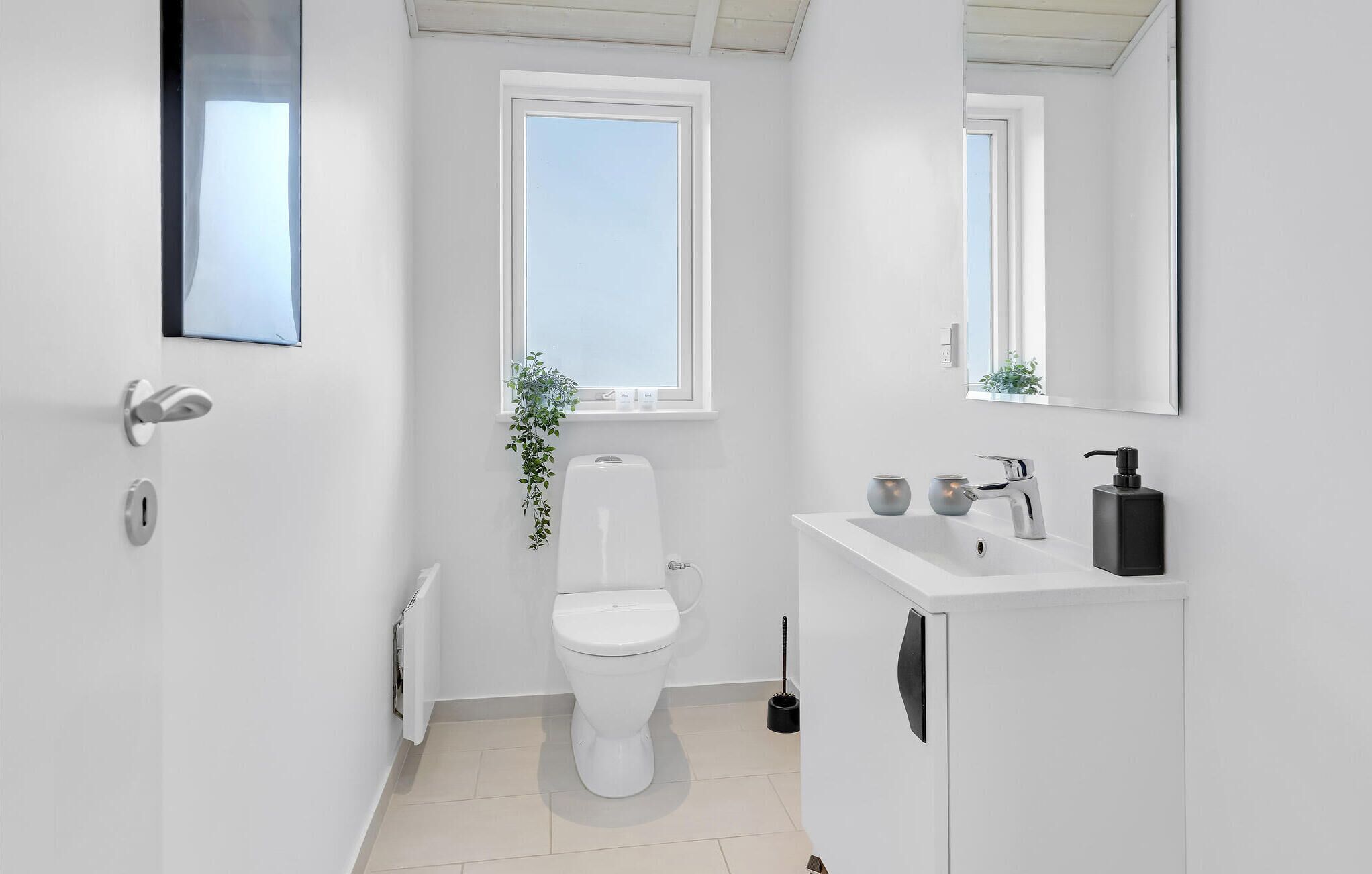 A modern bathroom with a toilet, a sink, a mirror, and a window.