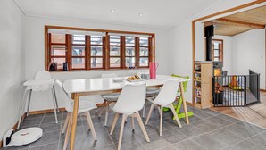 Zona pranzo con tavolo bianco, sedie e una finestra con stipiti in legno.