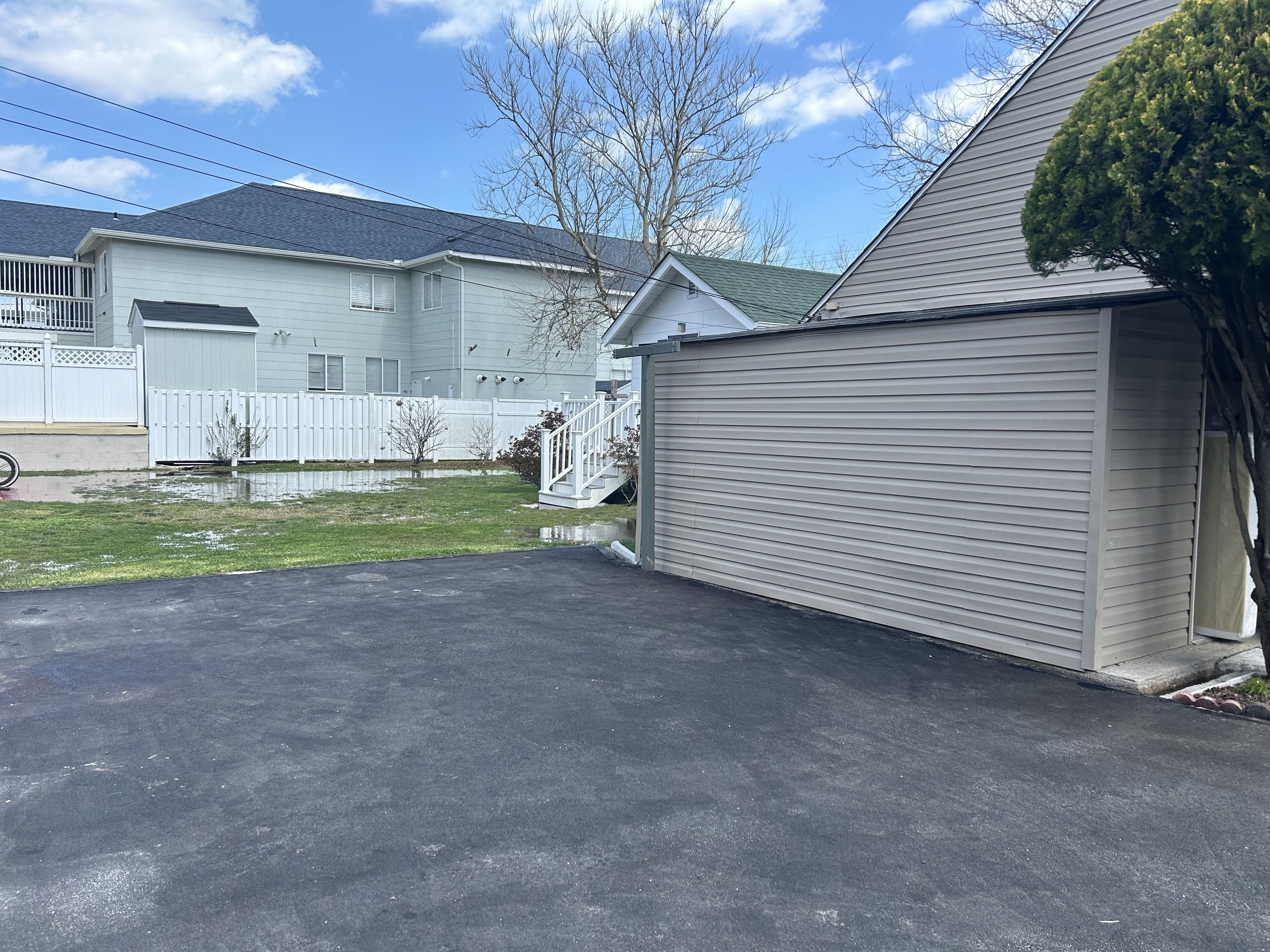 A residential driveway leading to a garage with a white fence and a tree.