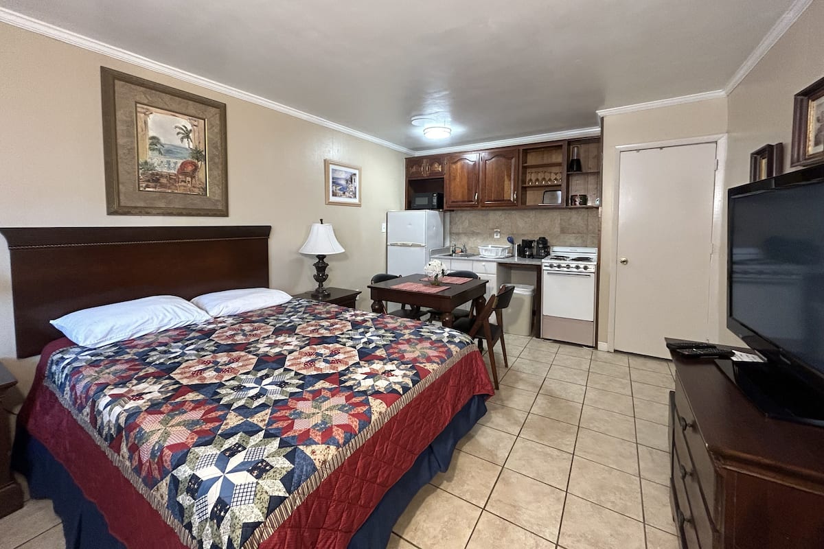 A hotel room with a bed, a desk, a kitchenette, and a television.