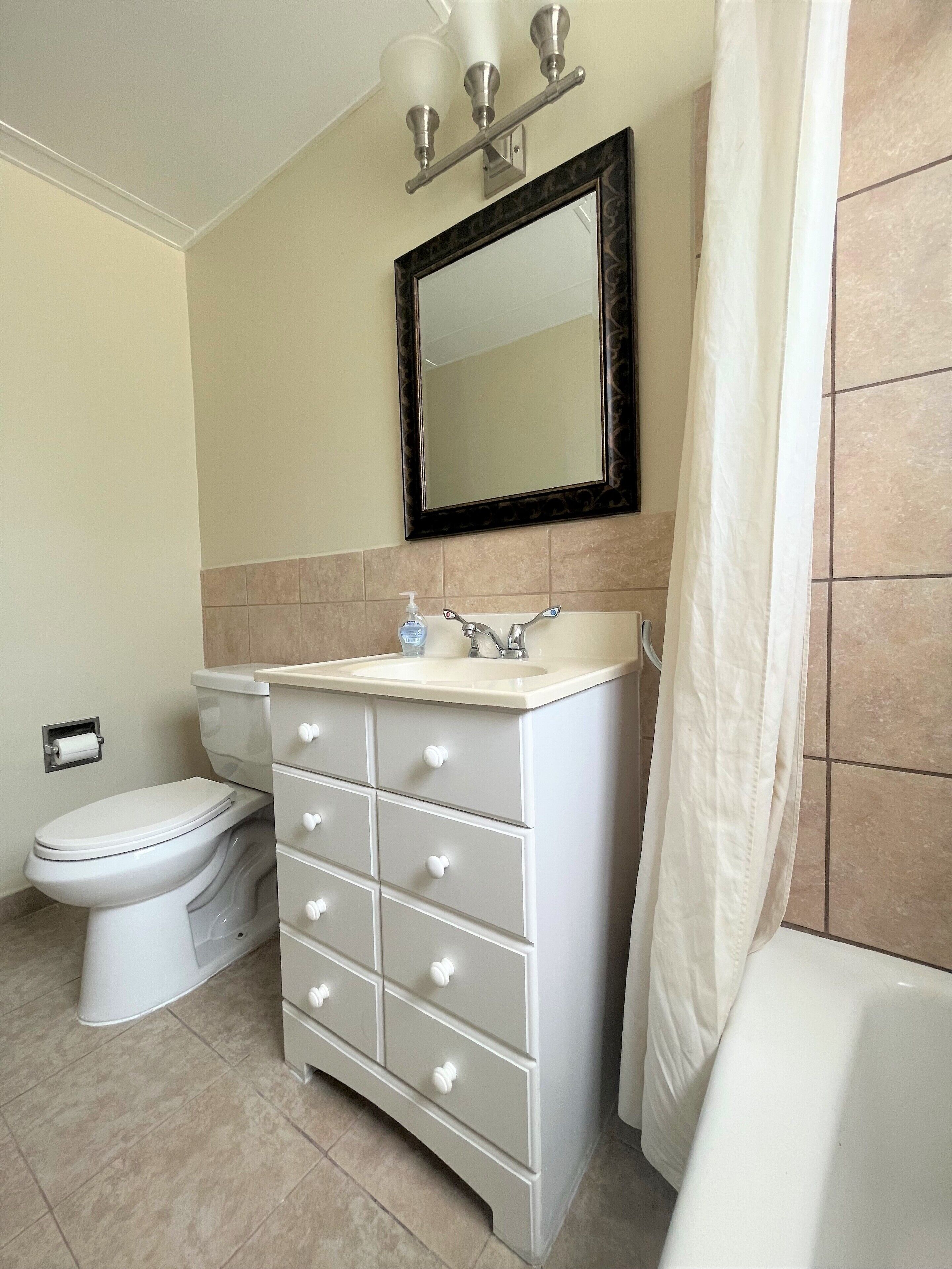 A bathroom with a toilet, a sink with a mirror above it, and a white cabinet with drawers.