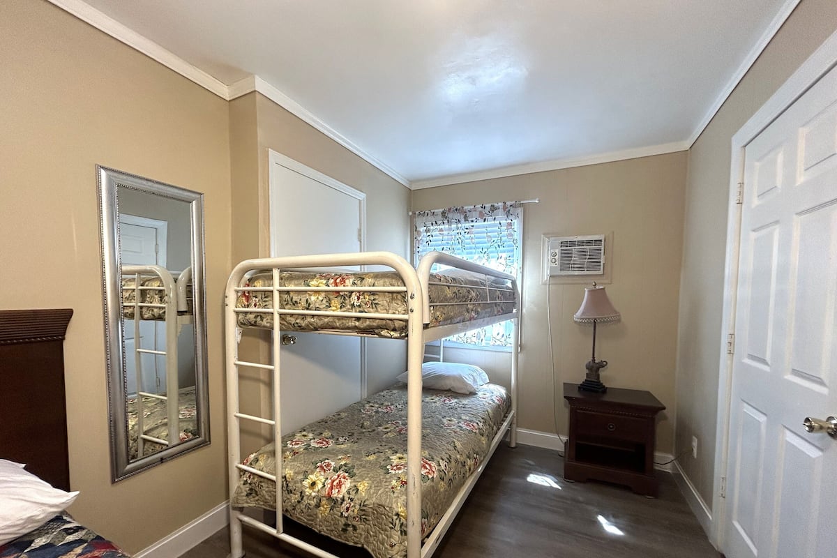 A room with a bunk bed, a mirror, a bedside table with a lamp, and a door.
