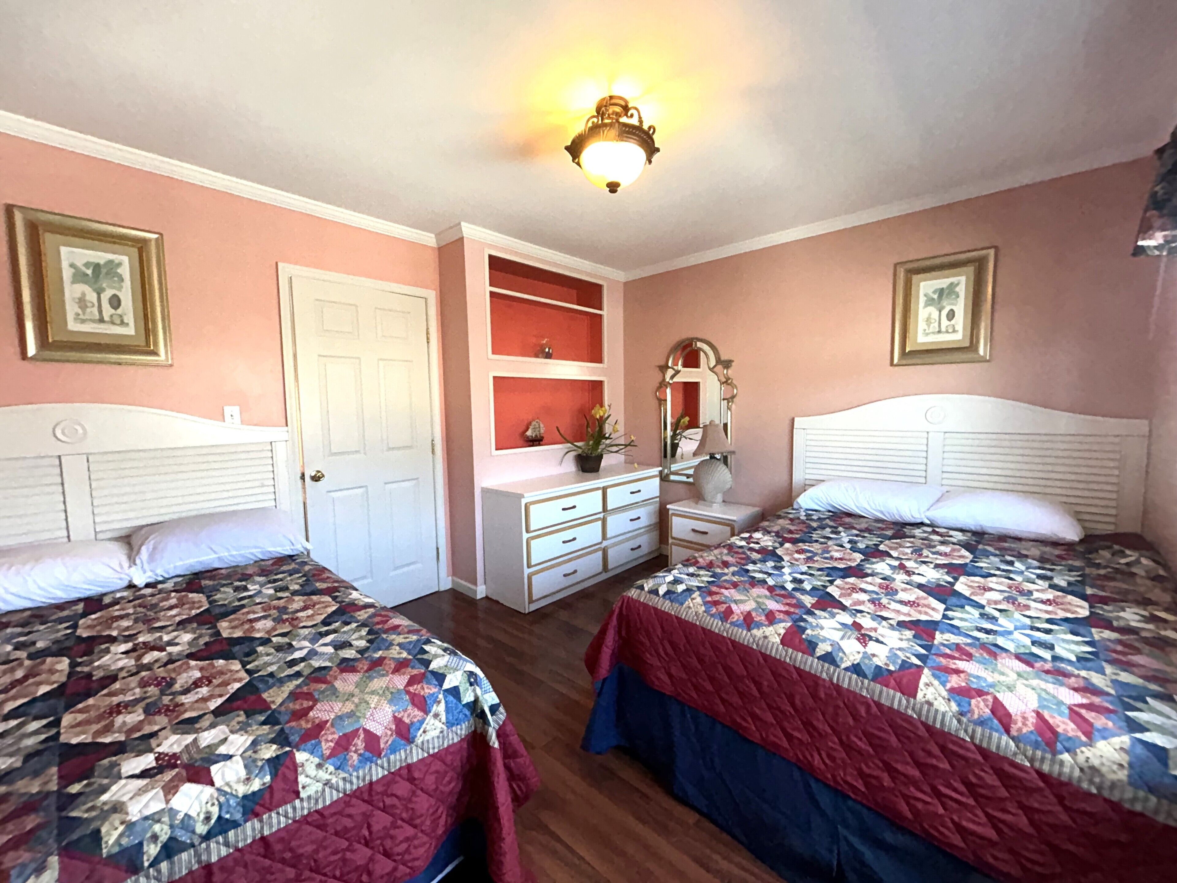A bedroom with two beds, a dresser, a vanity, and a door.