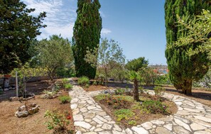 Stroll through the serene garden, surrounded by lush cypress trees and a variety of plants, along a winding stone pathway.