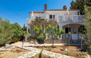 Enjoy a view of the surrounding area from the upper-floor balcony, surrounded by a lush garden with various plants and shrubs.