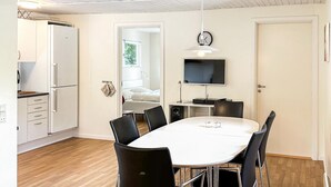 Een moderne keuken met witte kasten, een ingebouwde oven en een koelkast. Er is een eethoek met een ronde tafel en zwarte stoelen. Een flatscreen televisie is aan de muur boven de tafel bevestigd.