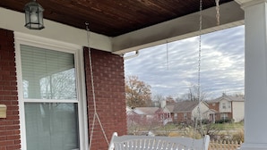 A covered porch with a white bench, a hanging lantern, and a brick wall.