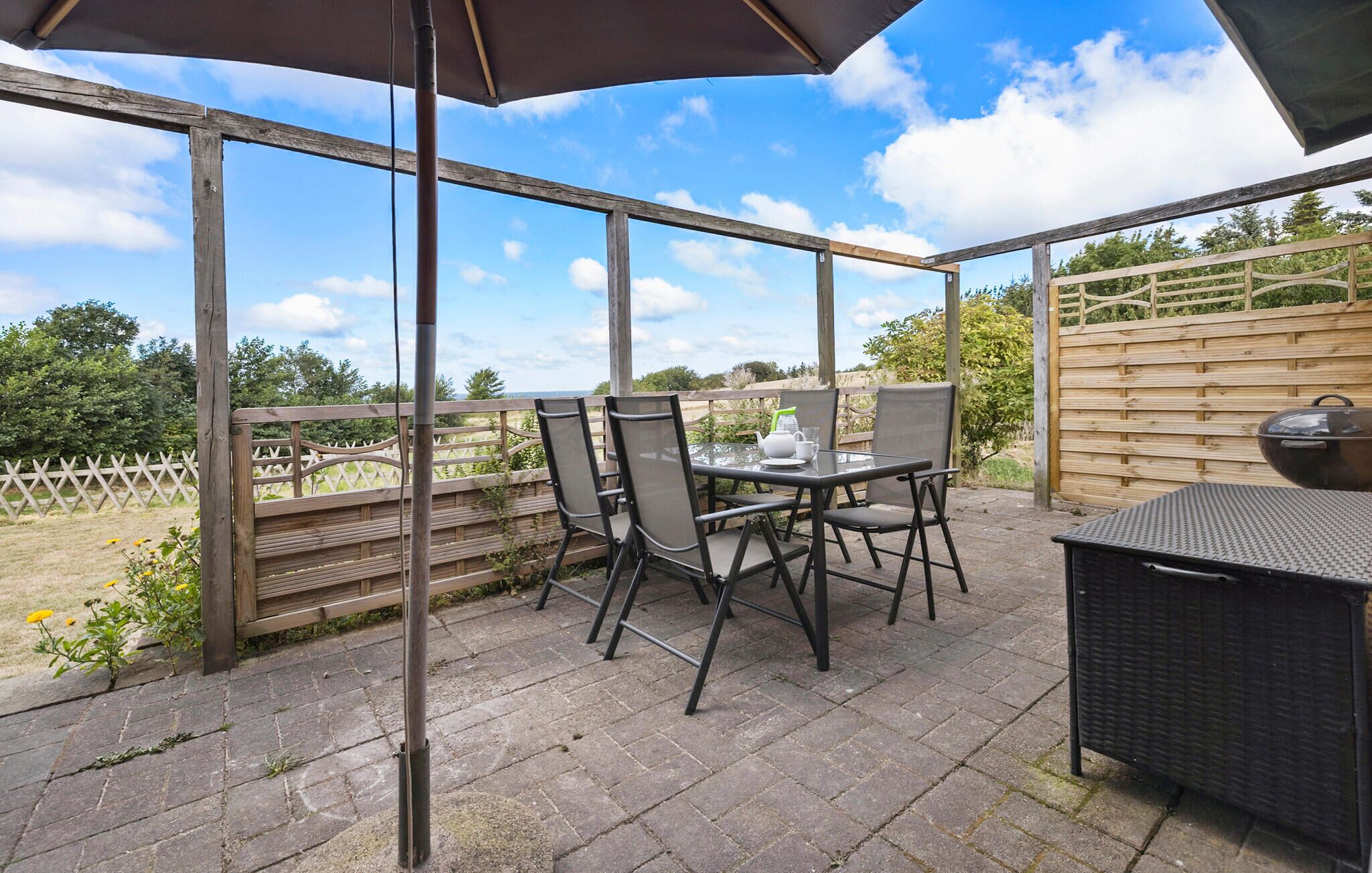 A covered patio area with a table and chairs, a grill, and a view of the surrounding garden.