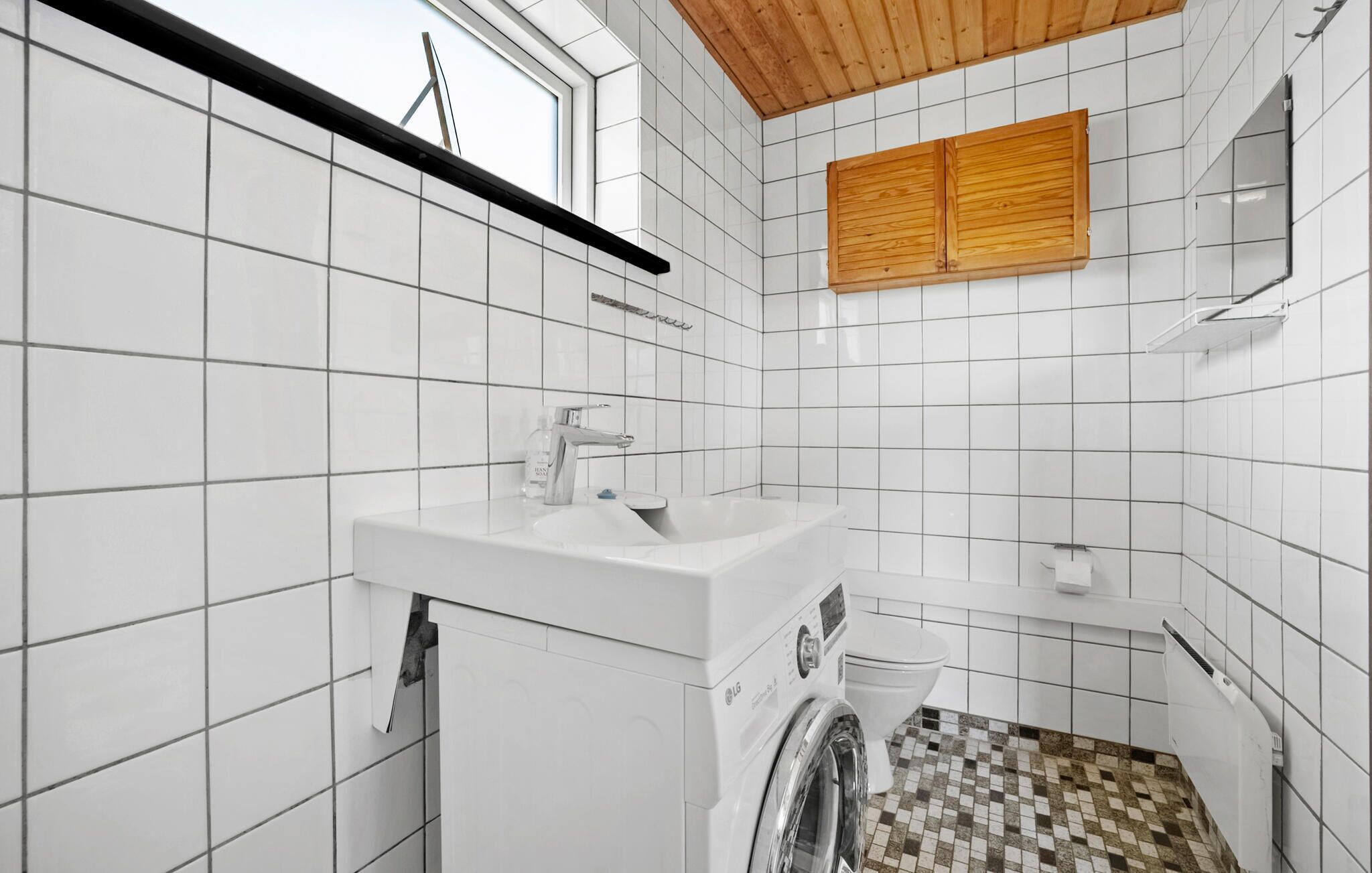 A bathroom with white tiled walls, a wooden ceiling, a sink, a toilet, and a washing machine.