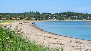 A beach with clear water, houses in the background, and a boat on the shore. - Lovely home in Fredericia with WiFi (Fredericia)